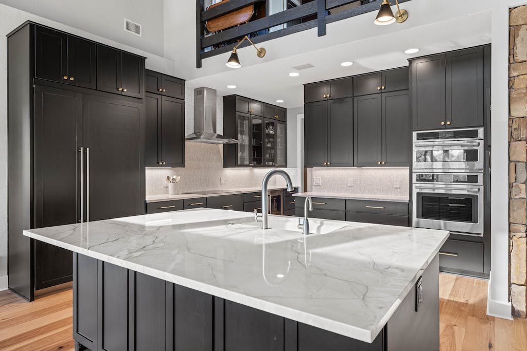 CliqStudios project: Black shaker kitchen cabinets with a white stone countertop and rustic beams above