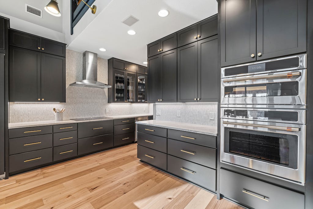 CliqStudios project: Black shaker kitchen cabinets with a white stone countertop and rustic beams above