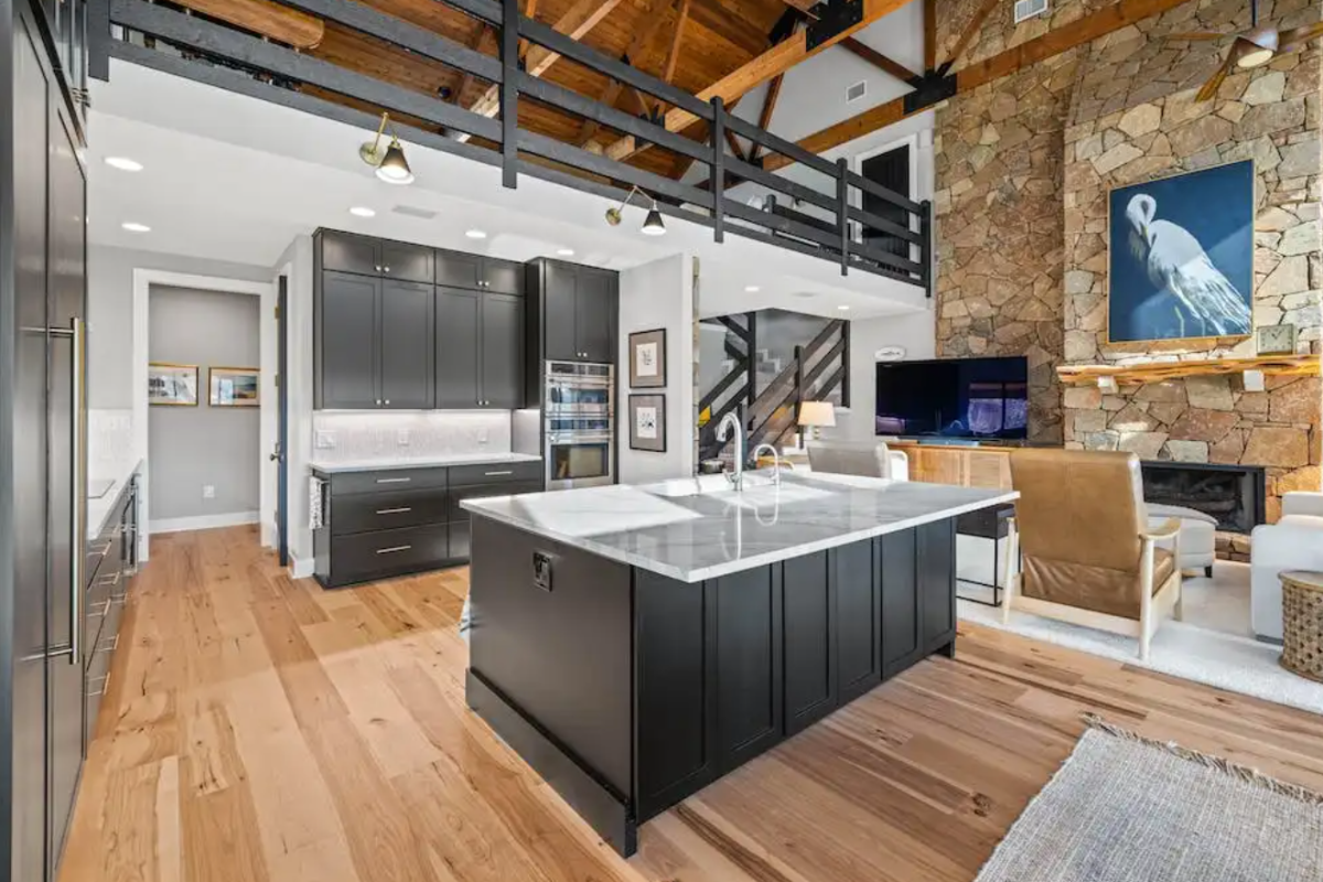 Large black kitchen design with stacked cabinets, white quartz countertops and rustic surroundings
