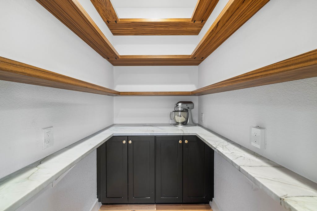 CliqStudios project: Black shaker pantry cabinets with a white wrap-around stone countertops and rustic floating shelves above