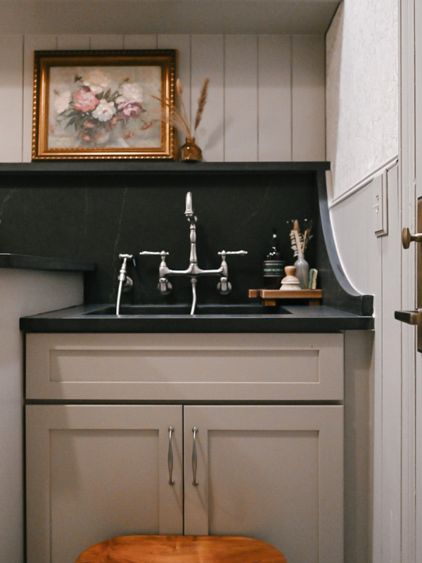 Light taupe shaker laundry room wall cabinets and sink base next to a washer/dryer and black quartz countertop