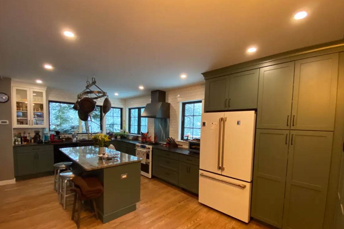 L-shaped dark green kitchen cabinet design with white and gold appliances and granite countertops