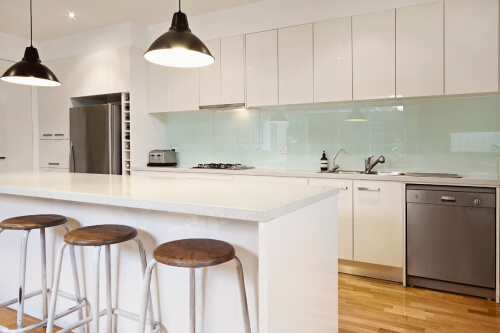 All white kitchen with high-gloss cabinets, light blue glass backsplash, white quartz countertops and black farmhouse pendant lighting