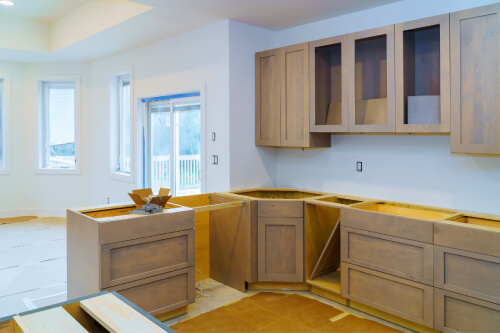 Light wood kitchen cabinets being installed in large white room