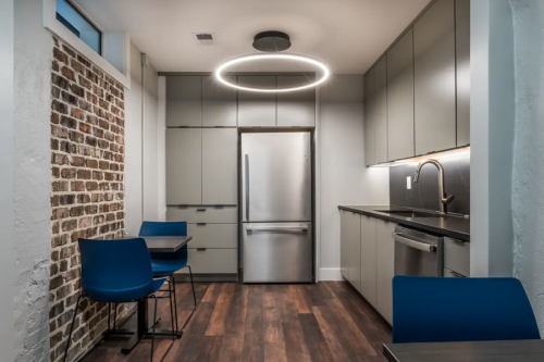 L-shaped dark gray slab door kitchen with stacked cabinets, modern black marble countertops and backsplash and modern led circle light fixture