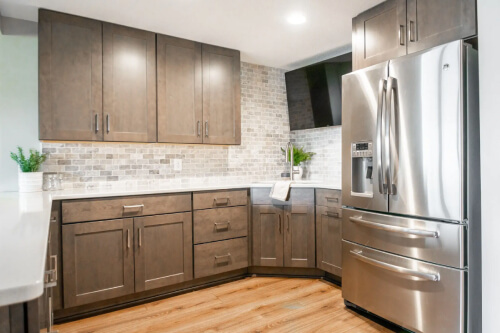 Medium wood tone U-shaped basement kitchen with shaker cabinets, brushed nickel hardware and a tonal tile backsplash