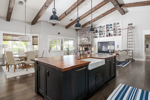 Large open kitchen and living room layout with black shaker island with butcher block countertops and a built-in white shaker entertainment center in the background with open cabinet storage above