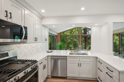 Light gray shaker-style kitchen with U-shaped peninsula design and black cabinet hardware