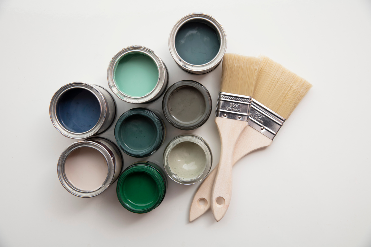 A group of low VOC paints in varying shades of green, gray, teal and pink with two paint brushes