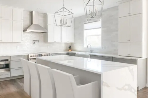 Large L-shaped white shaker style cabinet design with stacked cabinets, gray painted island and marble-like quartz countertops