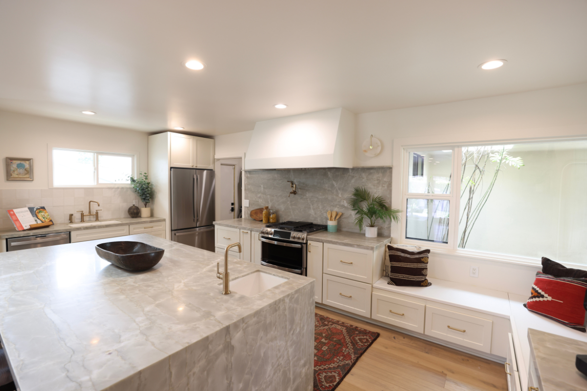 Mid-century modern cream shaker kitchen cabinet design with a large custom kitchen hood and medium wood-toned island cabinets with beautiful gray stone waterfall countertops