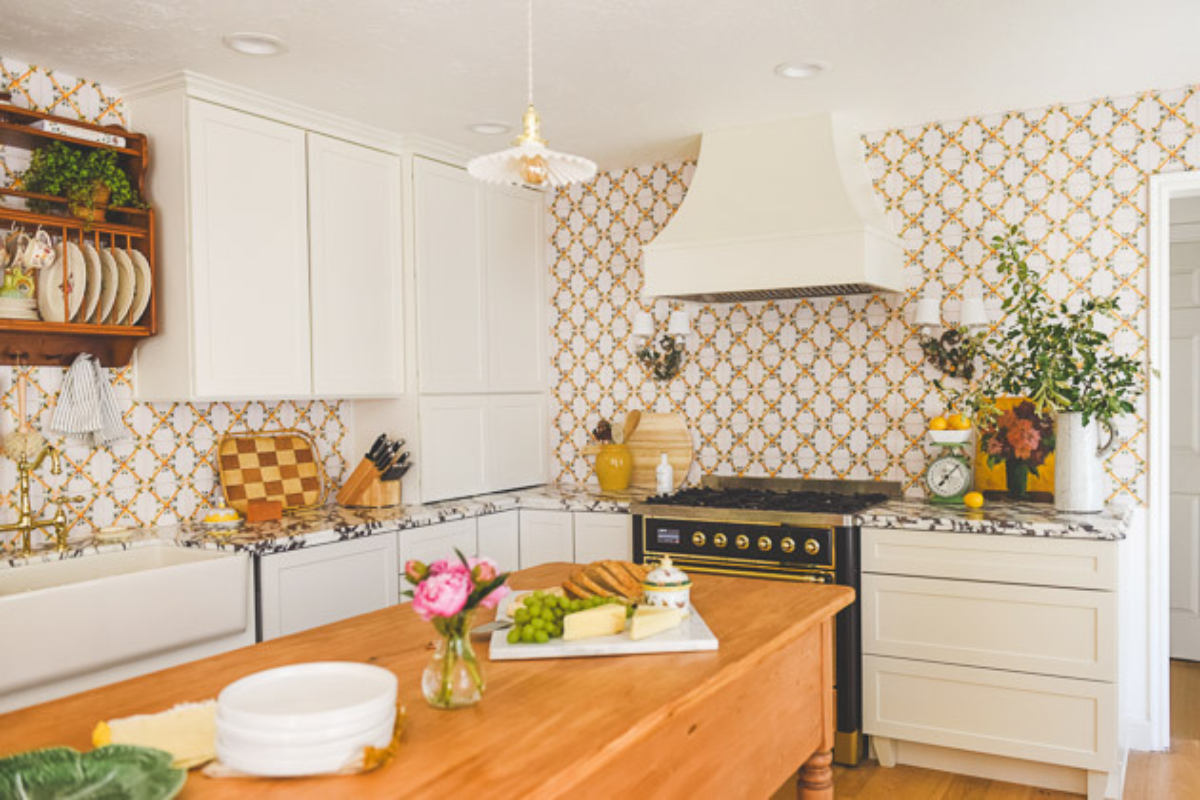 L-shaped cream shaker kitchen cabinet design with swedish influences, a matching wood kitchen hood, and vibrant orange and white tile backsplash