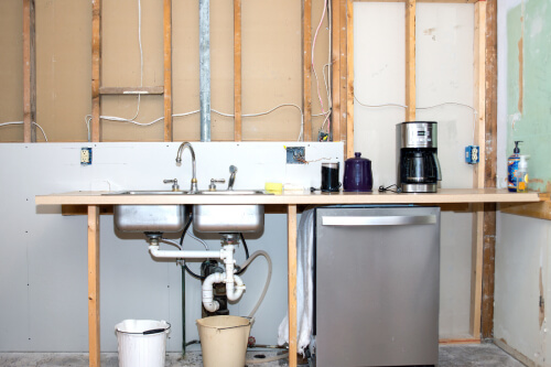 Temporary kitchen with a dishwasher, sink and coffee pot in front of stud construction