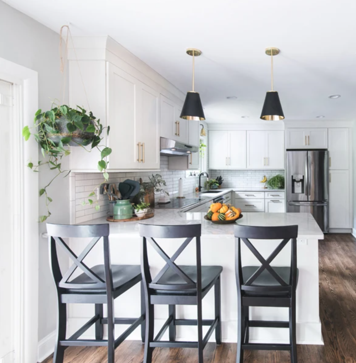 Long L-shaped white shaker-style kitchen and peninsula with gold hardware and black accents