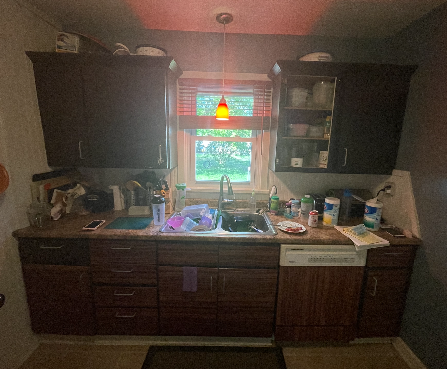 Over-crowded galley kitchen in dark and dingy finishes cluttered with household items 