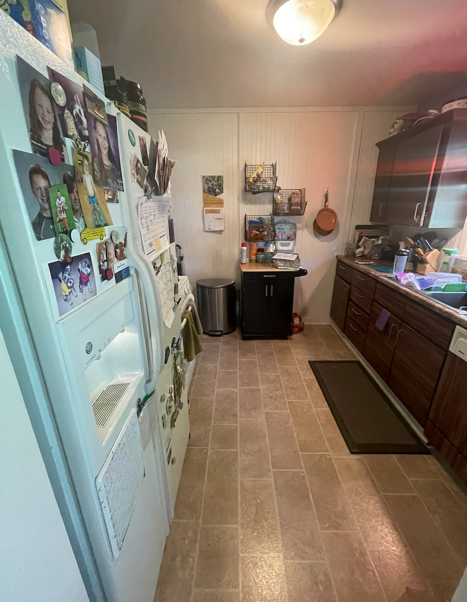 Over-crowded galley kitchen in dark and dingy finishes cluttered with household items 