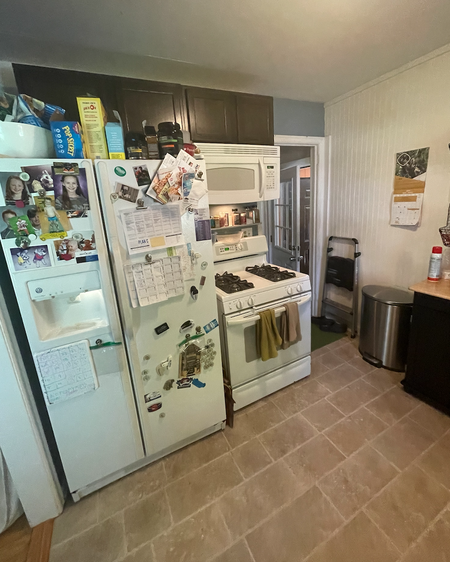 Over-crowded galley kitchen in dark and dingy finishes cluttered with household items 