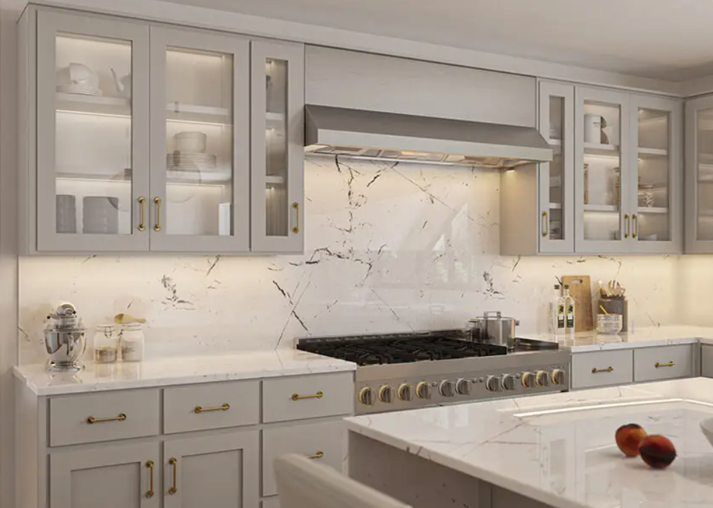 Light grey shaker kitchen cabinets with glass doors, gold hardware, and marble countertops