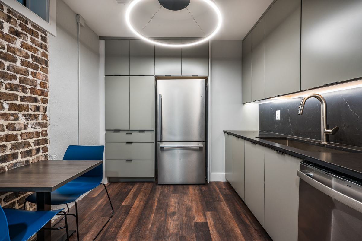 Gray slab door kitchen cabinets in Contemporary kitchen with black finger pulls, black marble slab backsplash and exposed brick in kitchen