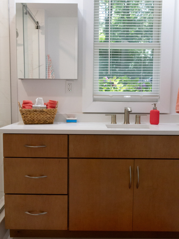 Warm wood tone vanity cabinet in a slab door style with white quartz countertops