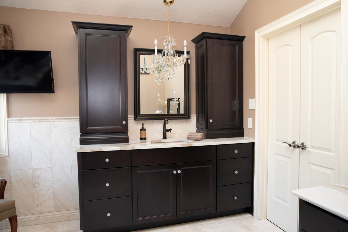 Dark espresso decorative vanity cabinet with tall wall cabinets on top of the cream-colored stone countertop