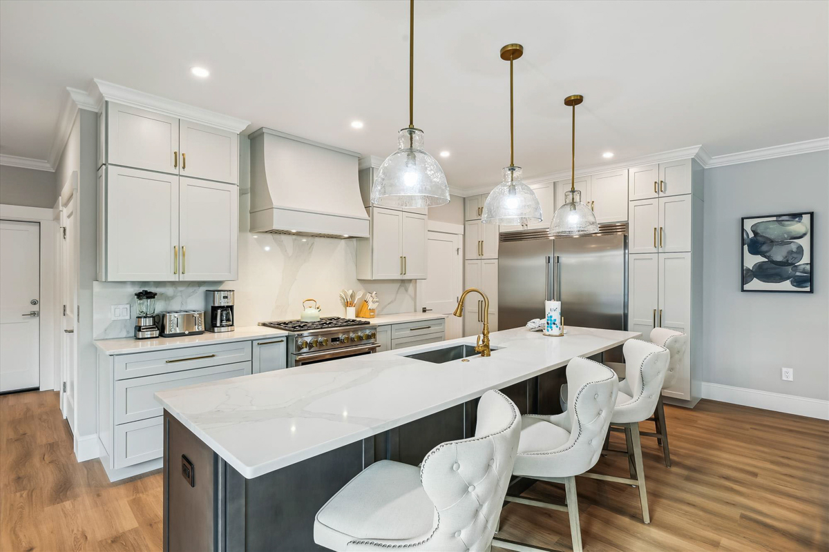 Large light gray shaker kitchen with matching wood hood, stacked cabinets with crown molding and a dark brown stained kitchen island