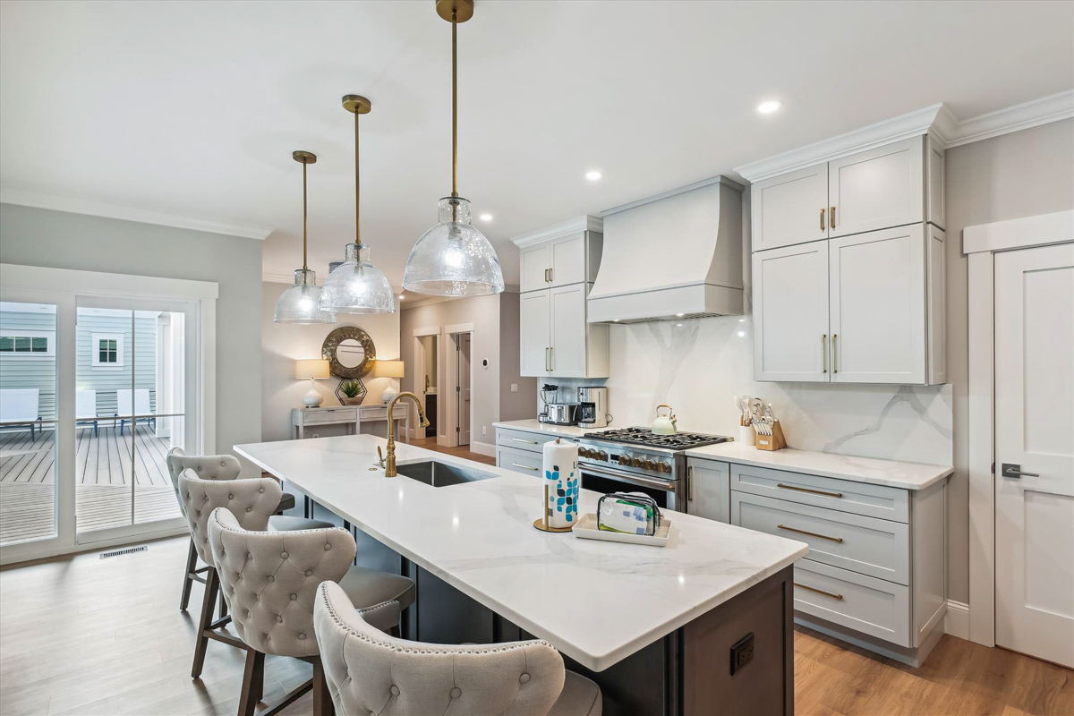 Large light gray shaker kitchen with matching wood hood, stacked cabinets with crown molding and a dark brown stained kitchen island