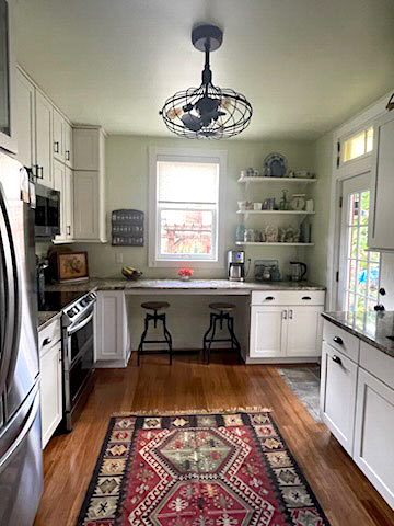 Stacked white kitchen cabinets with some glass inserts, floating wood shelves, and farmhouse accents and lighting