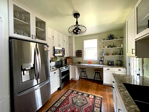 Stacked white kitchen cabinets with some glass inserts, floating wood shelves, a built-in desk, and farmhouse accents and lighting