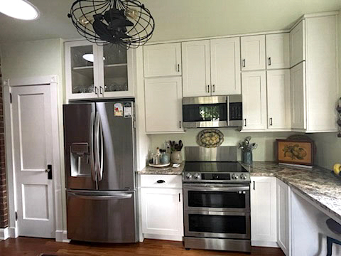 Stacked white kitchen cabinets with some glass inserts, floating wood shelves, a built-in desk, and farmhouse accents and lighting