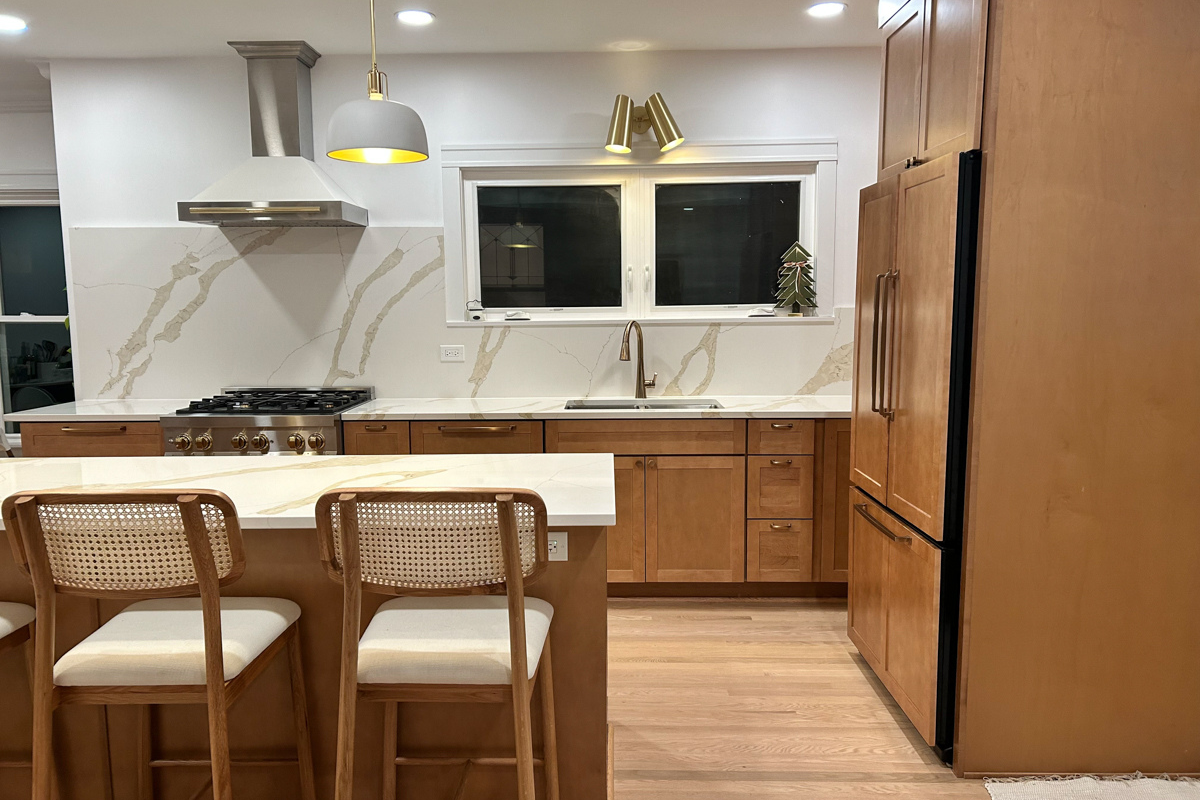 L-shaped mid-tone brown shaker kitchen with paneled refrigerator, large island with quartz countertops and matching slab backsplash