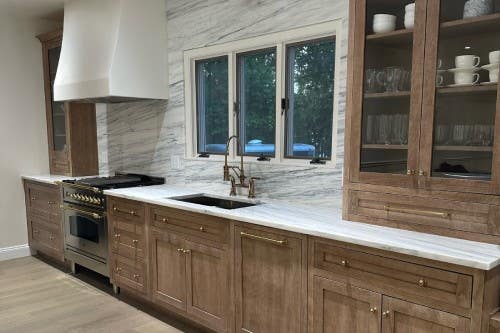 Transitional furniture-style kitchen design in light wood kitchen cabinets with gold hardware and white and blue countertops and matching slab backsplash