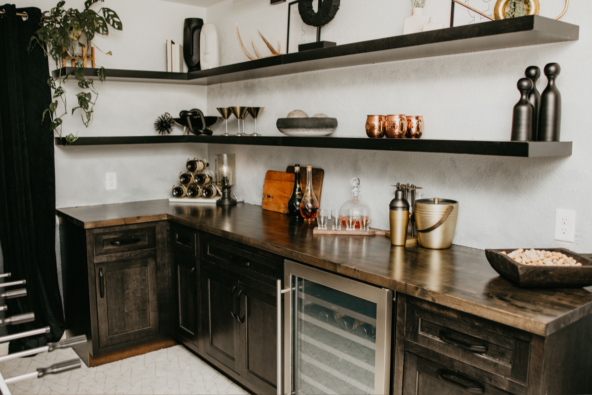 Dark brownish-black basement bar cabinets in inset cabinet style with floating shelves above