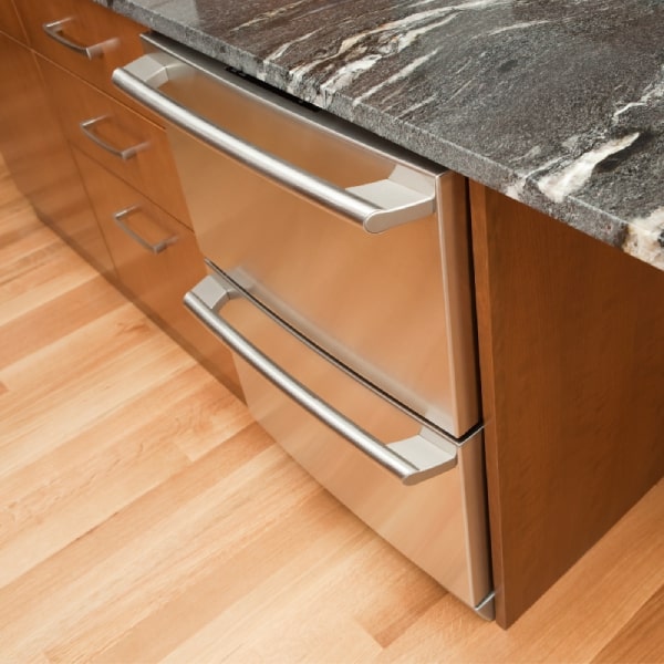 Two refrigerator drawers in a kitchen island with dark gray granite countertops