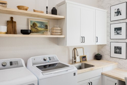 White shaker laundry room with butcher block countertops and wood floating shelves