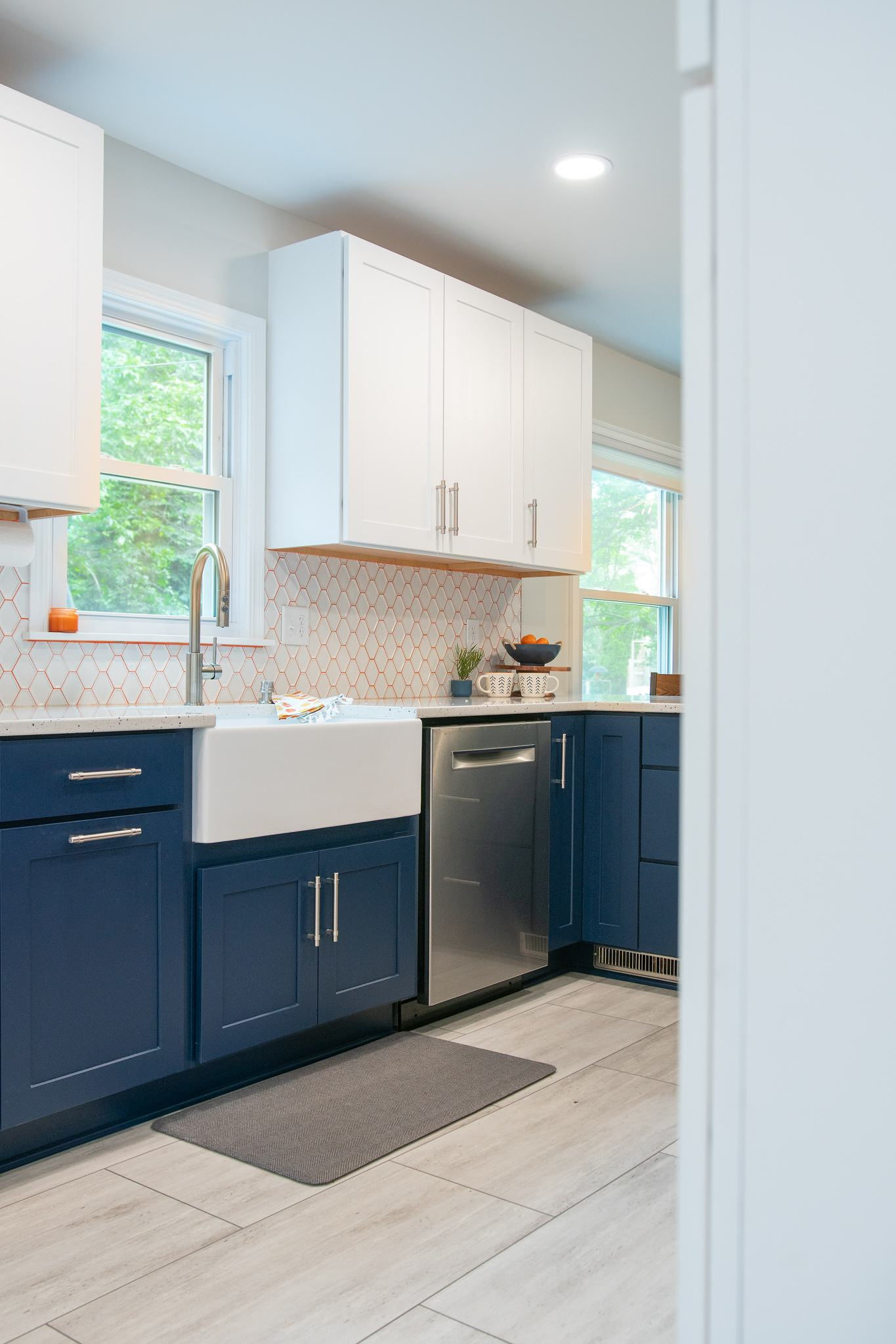 CliqStudios project: White and blue shaker kitchen cabinets with apron sink and white tile backsplash with orange grout