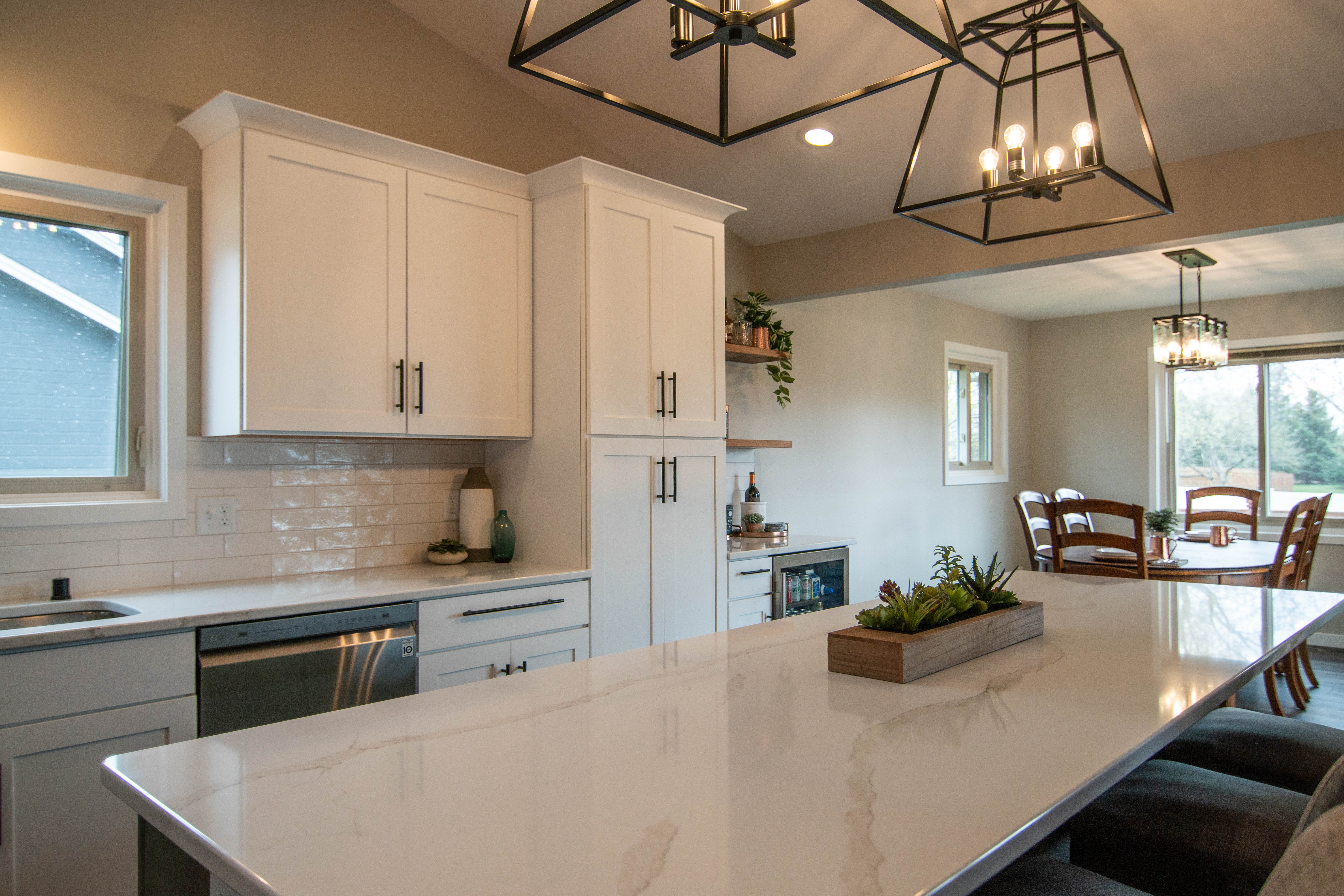 CliqStudios project: White shaker kitchen cabinets with a gray island, white quartz countertops and bronze accents