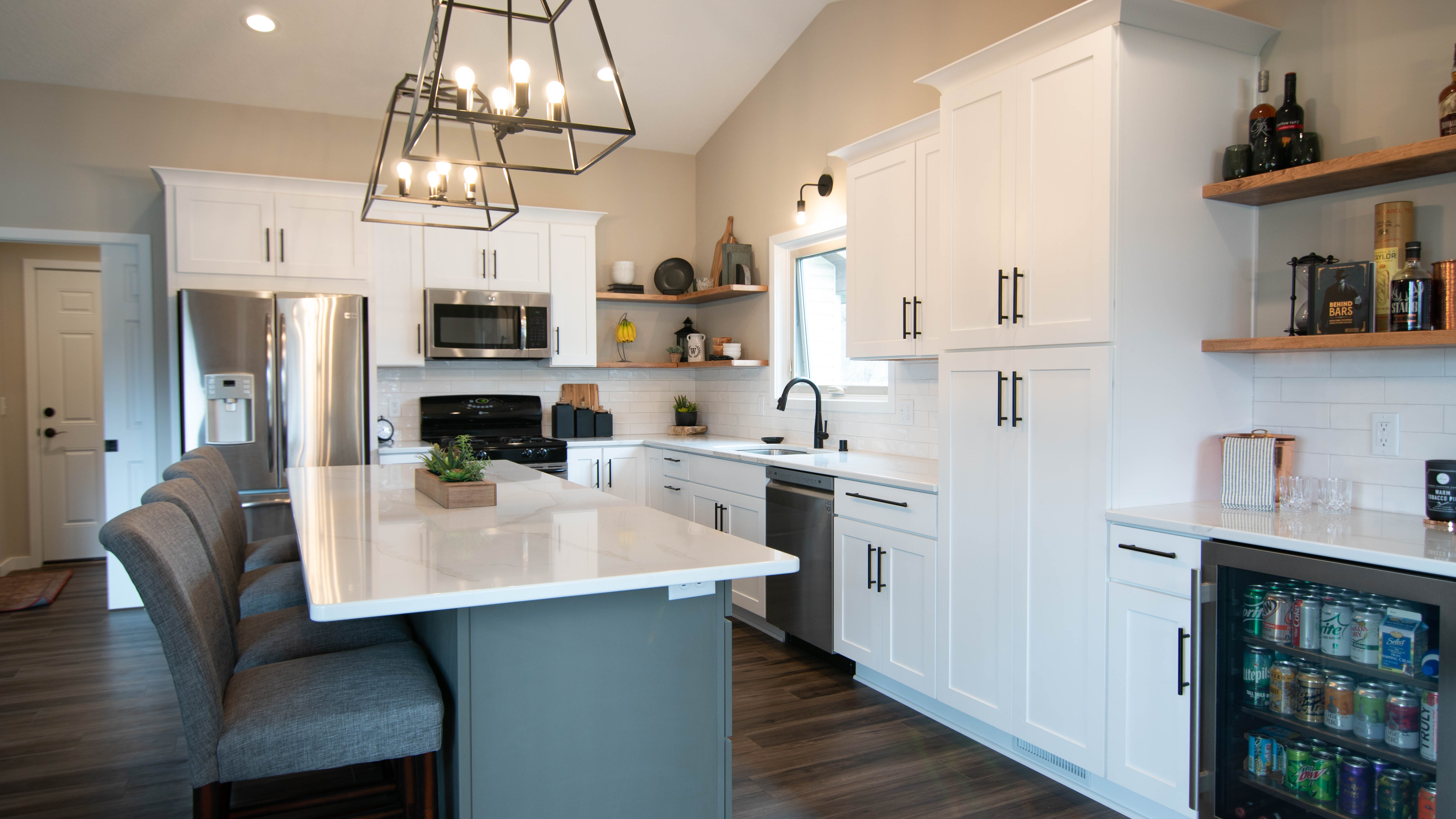 CliqStudios project: White shaker kitchen cabinets with a gray island, white quartz countertops and bronze accents