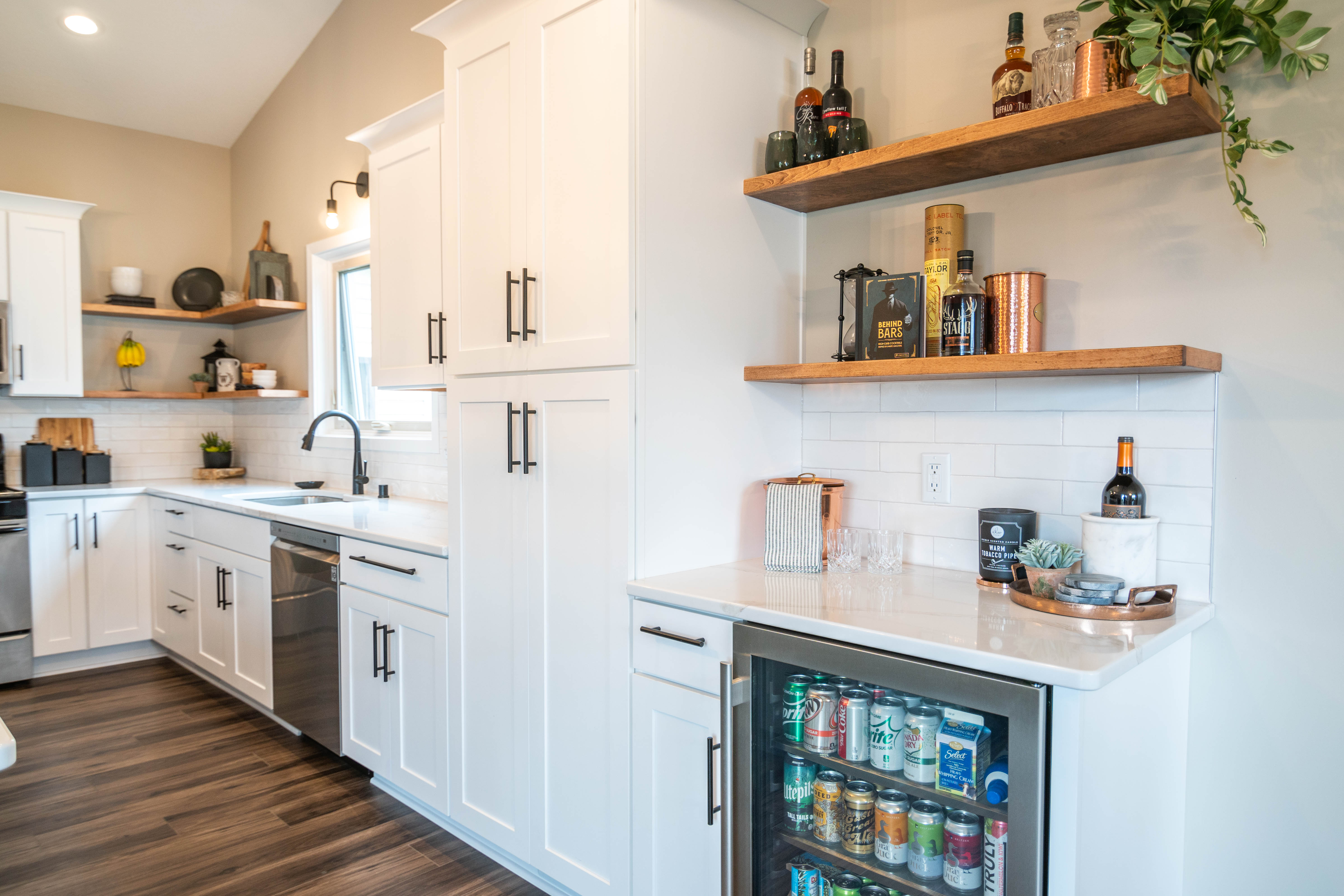 CliqStudios project: White shaker kitchen cabinets with a gray island, white quartz countertops, wood floating shelves, and bronze accents