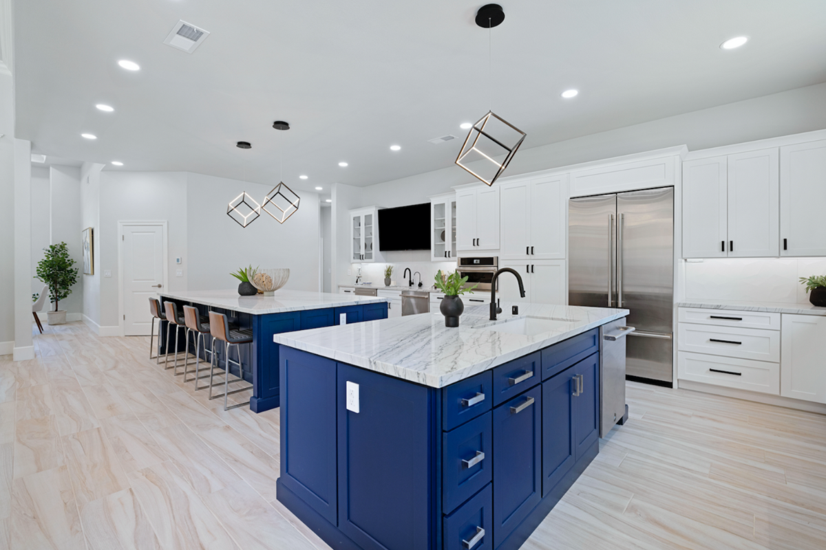 White shaker kitchen cabinets with two navy blue kitchen islands and white quartz countertops