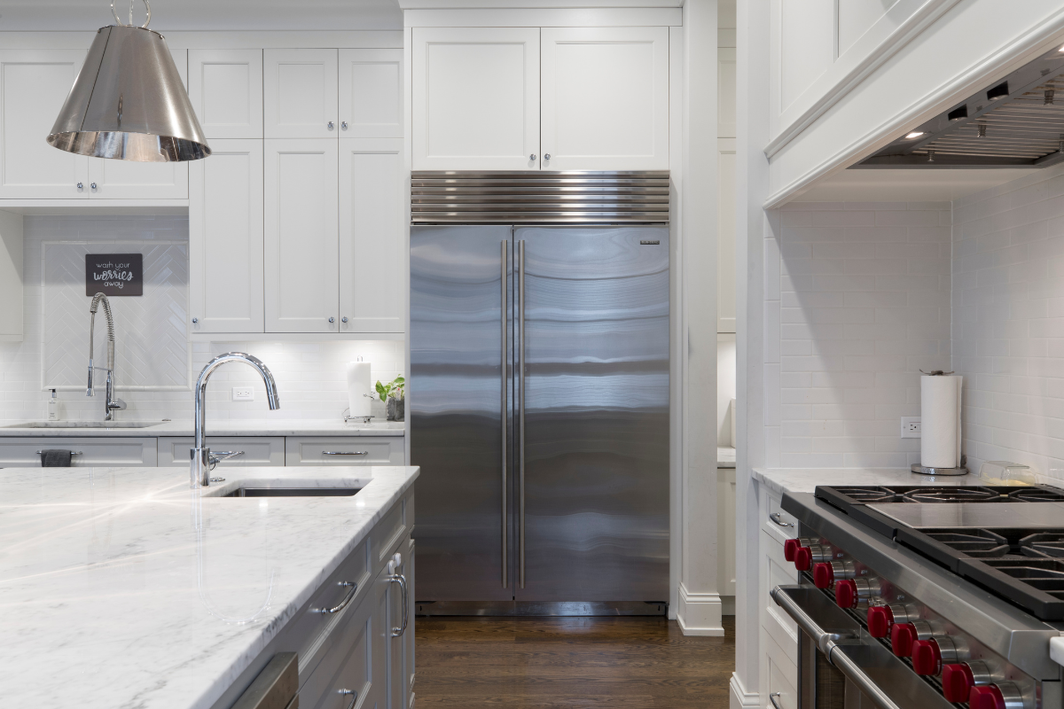 White inset shaker kitchen cabinets in a large luxurious kitchen design with a built-in professional-grade stainless steel refrigerator