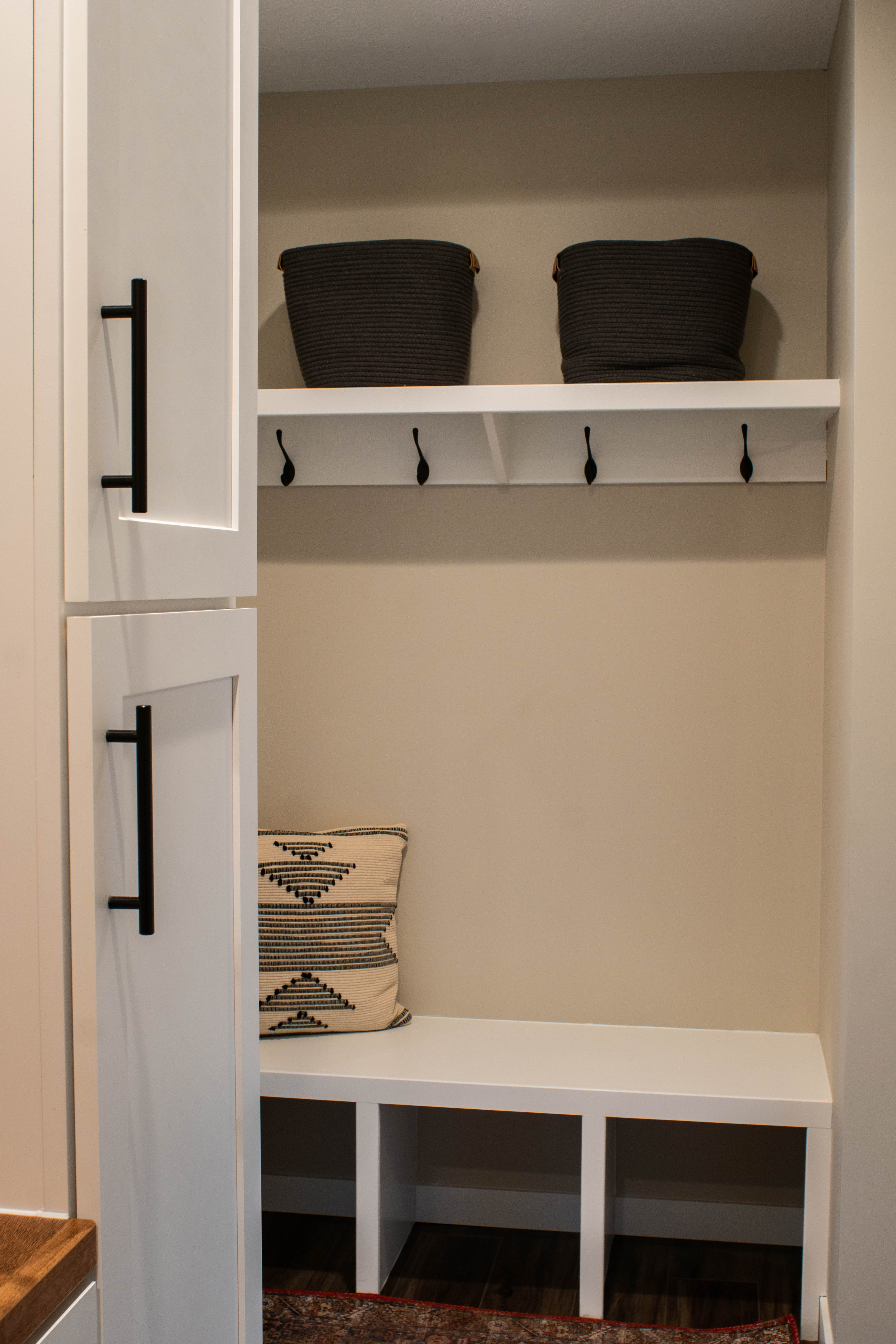 CliqStudios project: White laundry and mudroom cabinets with warm golden wood floating shelves and a mudroom bench