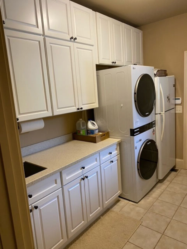 Stacked white laundry room cabinets with raised panel door style and tan countertops