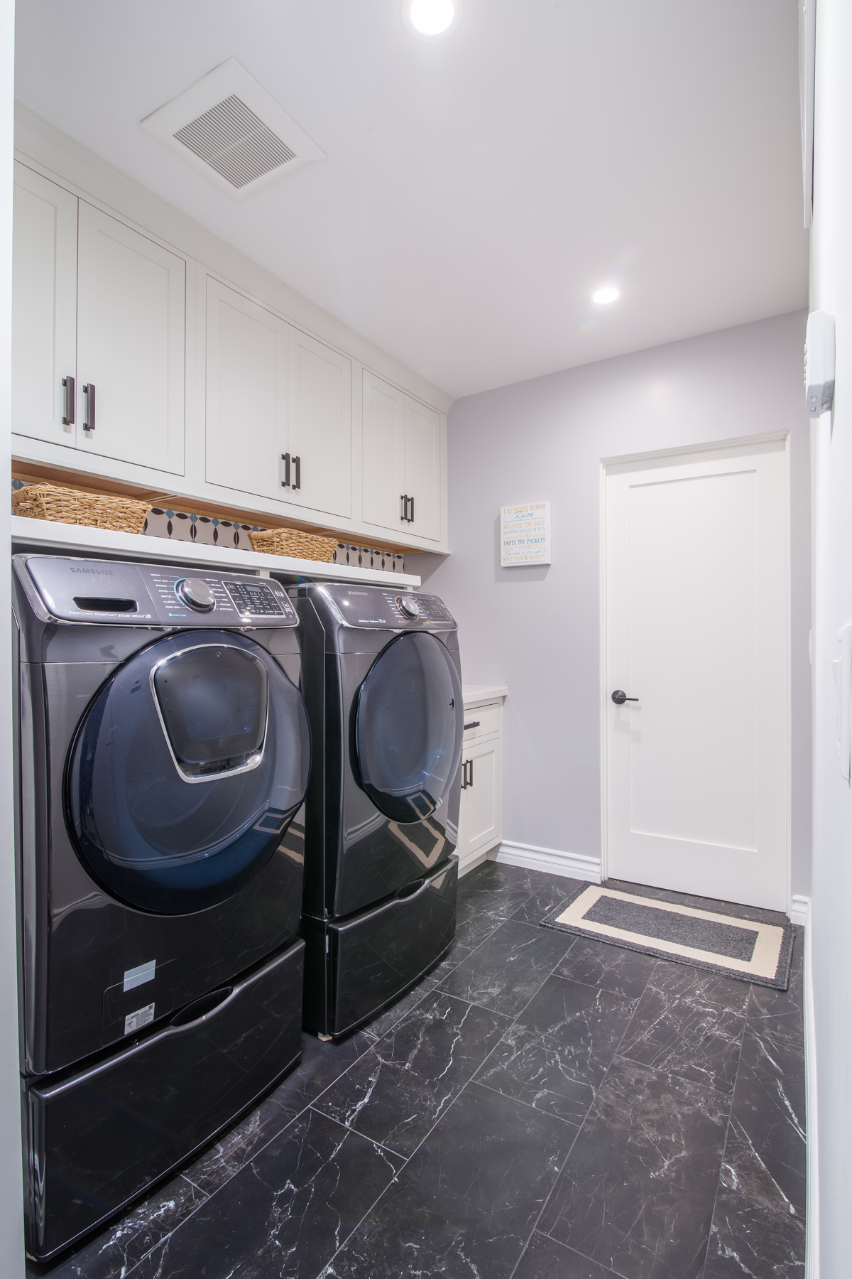 This image is of frontload washer and dryer set placed under the white laundry room cabinets.