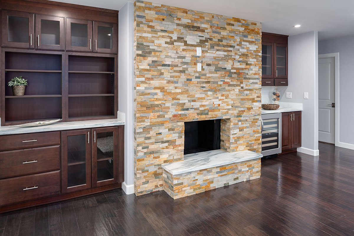 fireplace surround created by bookshelf walls of cherry cabinets in Bayport raised panel style with glass doors and slab-front drawers and builtin beverage cooler