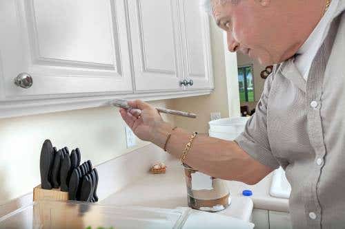 Man hand-painting white raised panel wall cabinets with chrome knobs 