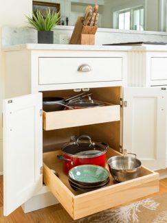 Double roll-out trays storing bowls, pots, and a colander. Featuring an White inset styled base cabinet