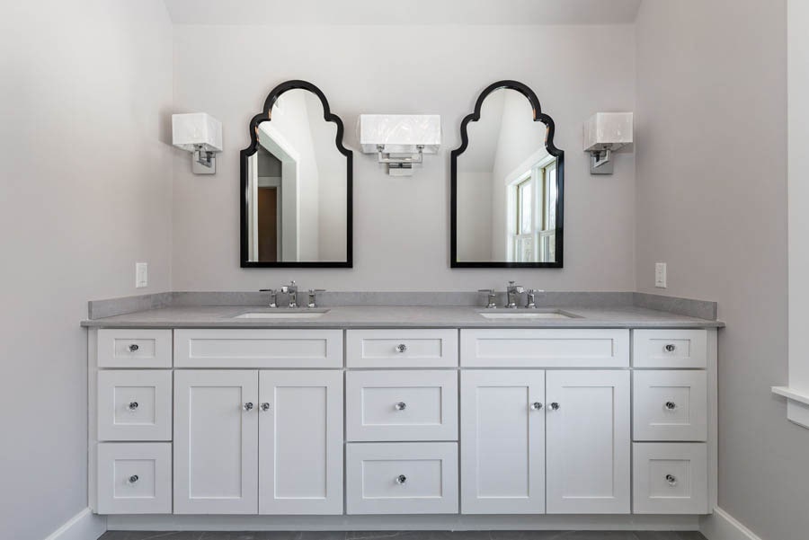 Gray master bathroom with a double-sink white shaker bathroom cabinet with drawers and decorative black framed mirrors