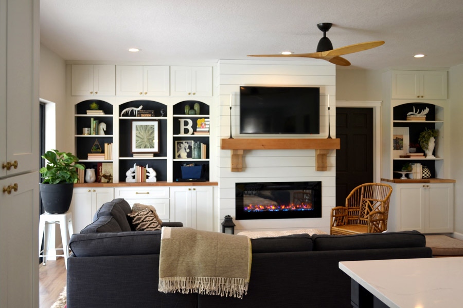 Living area using CliqStudios Shaker cabinets in White around the entertainment area for added storage. Base cabinets have butcher board countertops, above them is open air shelving, and flush with the ceiling are more small cabinets.