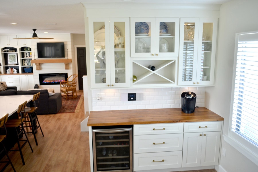 CliqStudios Dayton cabinets in white forming a butler's pantry, with a wine cooler in the base and a wine rack above centered in glass faced cabinets.